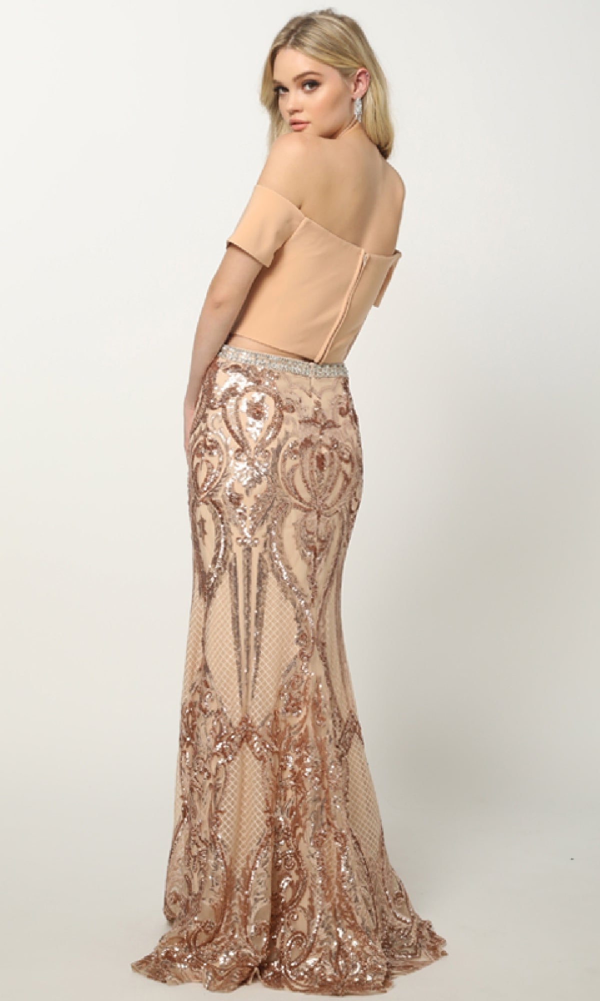 Woman wearing the Juliet 663 beige off-the-shoulder long prom dress with a sequin print skirt and mesh detailing, standing and looking over her shoulder against a plain background.